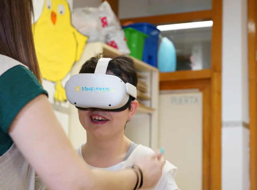 Una educadora acompaña en el aula a una alumna que lleva puestas las gafas de realidad virtual de Minifunkids