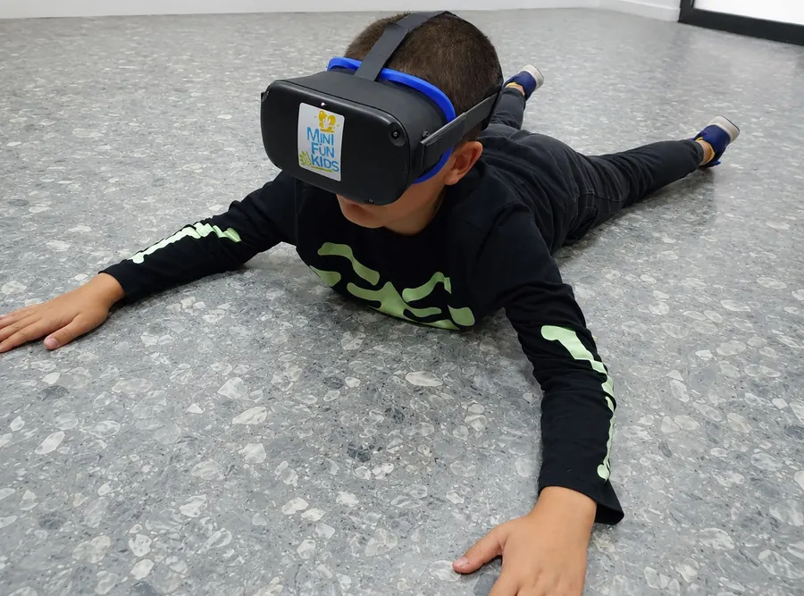 Un niño tumbado en el suelo con las gafas de realidad virtual de Minifunkids extiende brazos y piernas mientras explora la experiencia