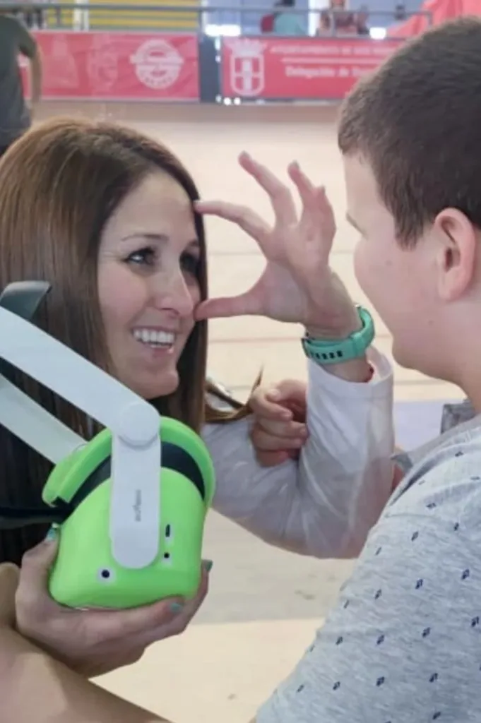 Una profesional de Minifunkids sujeta unas gafas de realidad virtual mientras acompaña a un niño en una jornada inclusiva