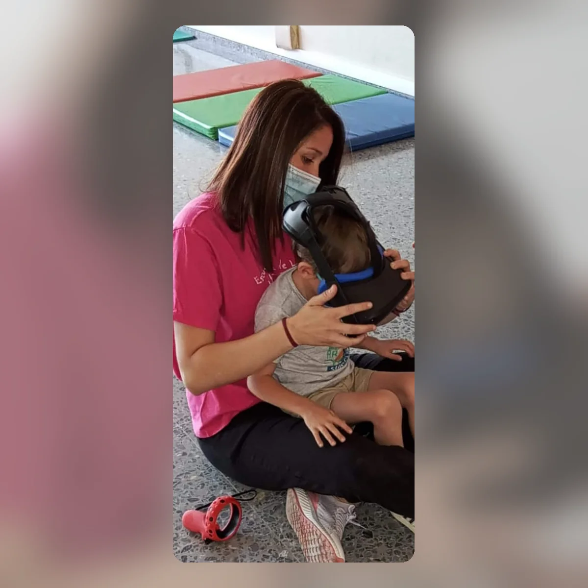 Una profesional sentada en el suelo de una sala coloca con cuidado las gafas de realidad virtual a un niño que tiene sentado en su regazo