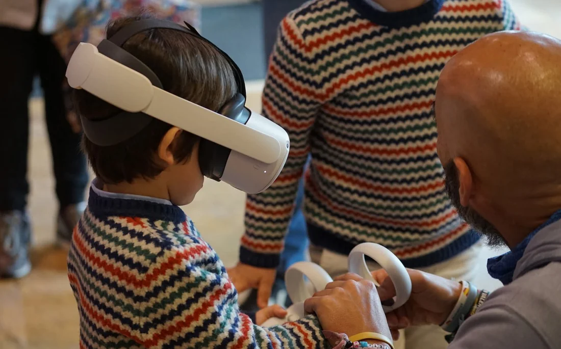 Un adulto guía las manos de un niño con los mandos de realidad virtual mientras él lleva puestas las gafas Minifunkids