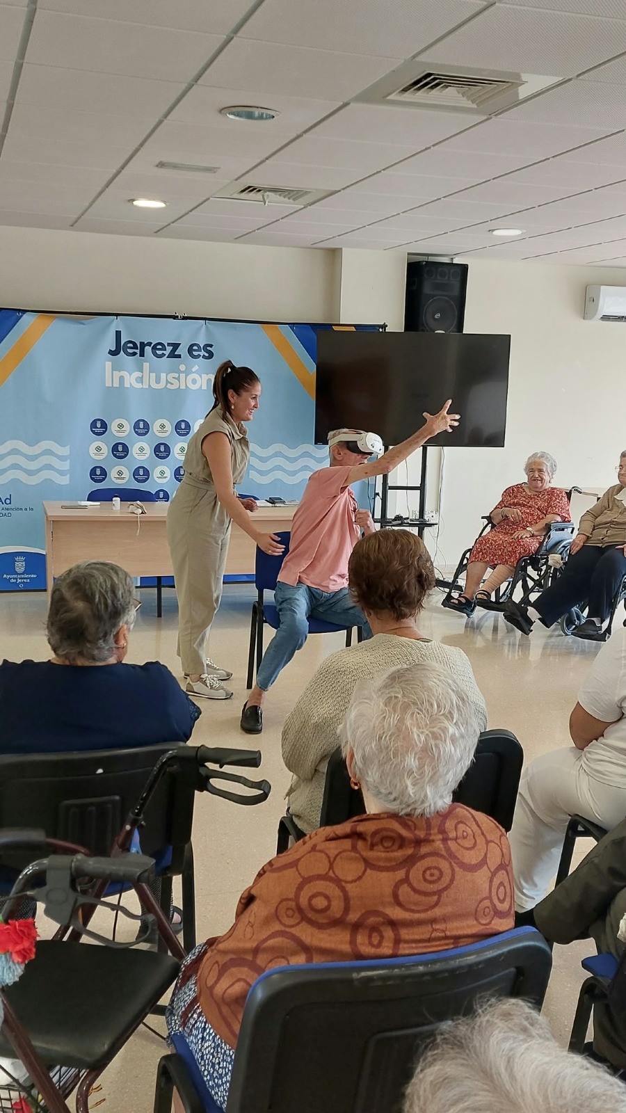 Un participante mayor levanta el brazo durante el taller de realidad virtual en Jerez, ante el grupo