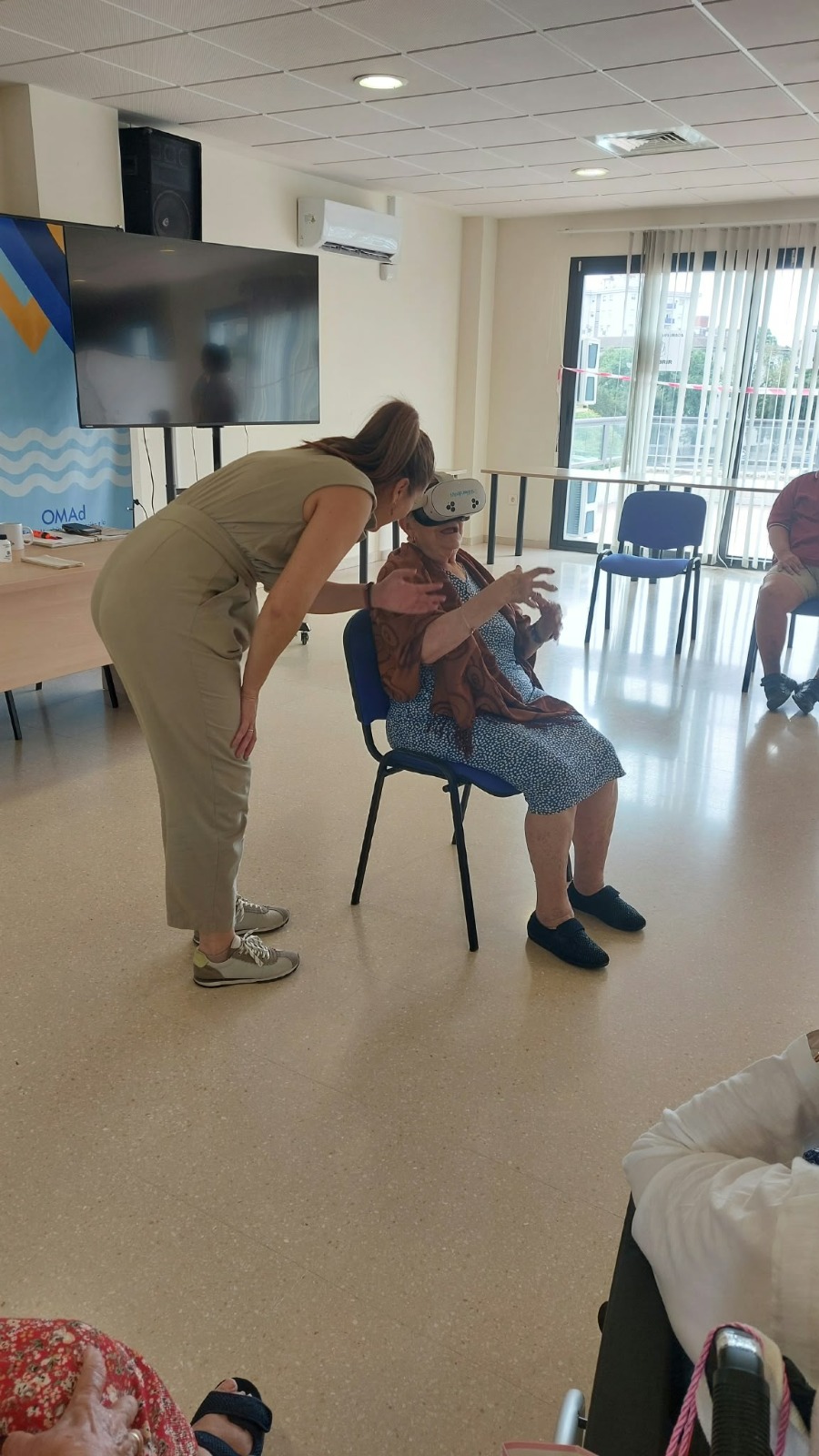 Una monitora de Minifunkids acompaña de cerca a una mujer mayor sentada con gafas de realidad virtual en Jerez